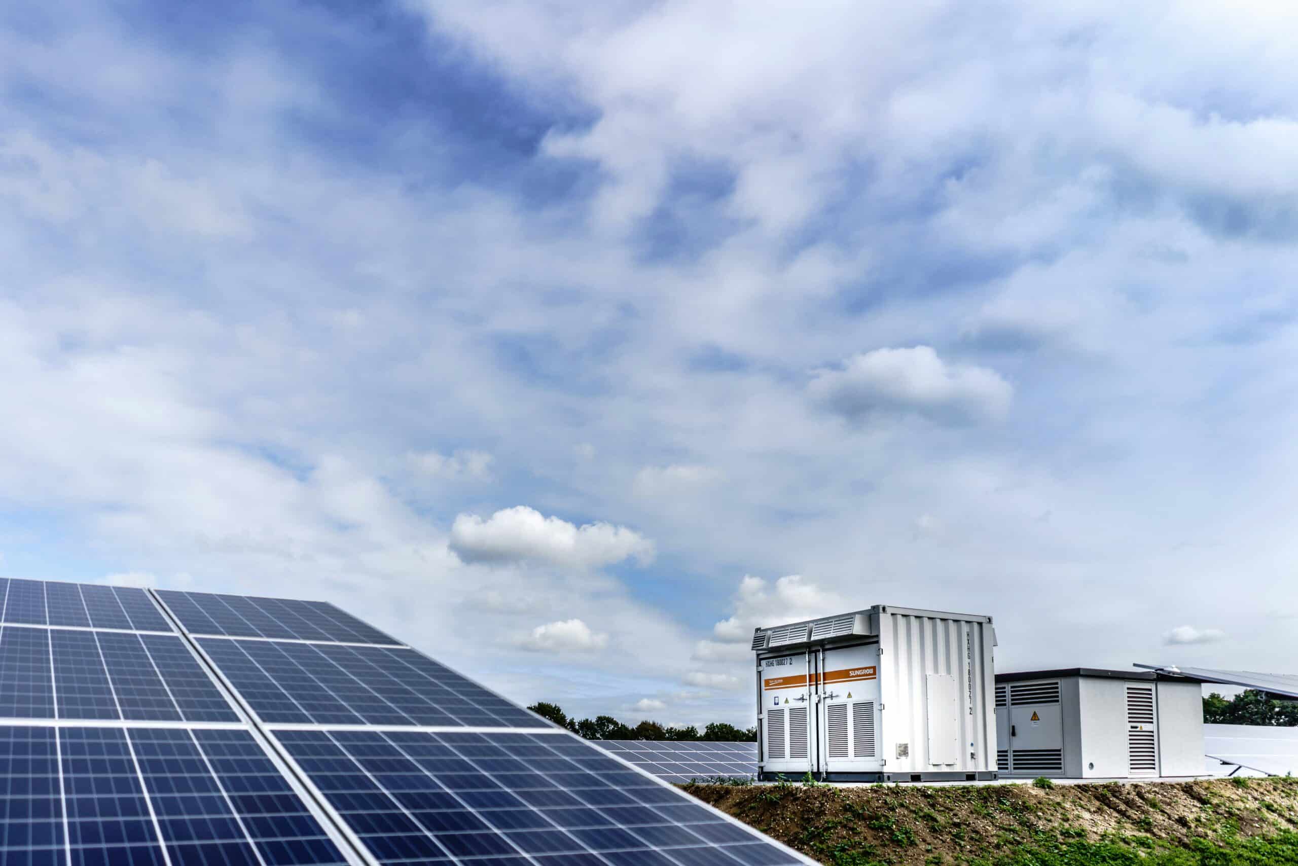 Solar panels installed on a hillside, with a building visible in the background under a clear blue sky.